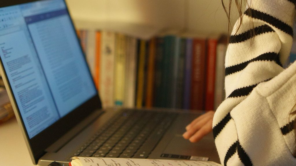 Estudante concentrada estudando em uma mesa de casa com laptop e livros