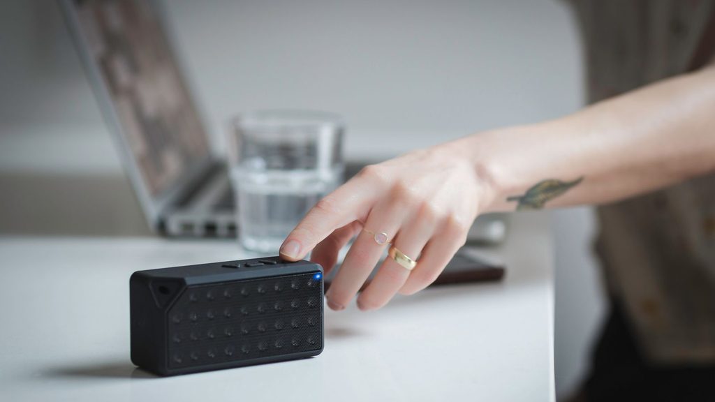 Caixa de som ao lado de teclado e notebook em mesa de trabalho